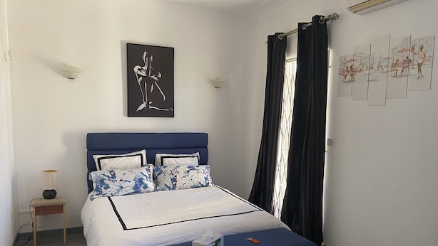 A bedroom with a bed, a nightstand, a lamp, a window with curtains, and a wall with artwork. - 3 Bedroom Private vacation home in Pereybere (Pereybere)