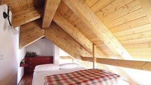 Une chambre avec un plafond en bois, un lit recouvert d’une couverture à carreaux, une commode et une petite plante.