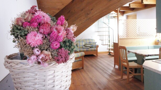 Une pièce chaleureuse avec un plafond en bois, un panier en osier rempli de fleurs, un canapé et une table à manger.