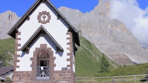 Une petite chapelle ornée d’une croix sur la façade, entourée d’un paysage montagneux.