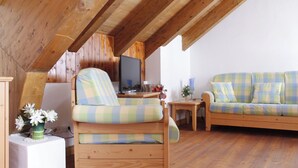 Une pièce chaleureuse avec un plafond en bois, un canapé, un fauteuil et une petite table sur laquelle est posé un vase de fleurs.