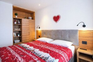 A bedroom with a bed, wooden wardrobe, shelves with books and plants, a heart-shaped decoration, and wall-mounted lights. - Casa Ibex - Residence with pool (Cavalese)