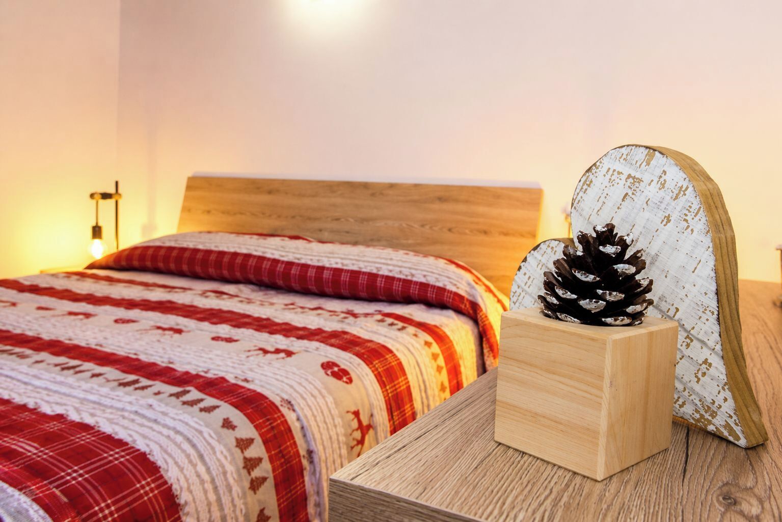 A neatly made bed with a red and white patterned bedspread, a wooden headboard, and a pine cone on a wooden block.