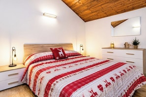 Ein Schlafzimmer mit Holzboden, einem Bett mit rotem und weißem Muster, Nachttischlampen, einem Nachttisch, einer Kommode und einem Spiegel an der Wand.