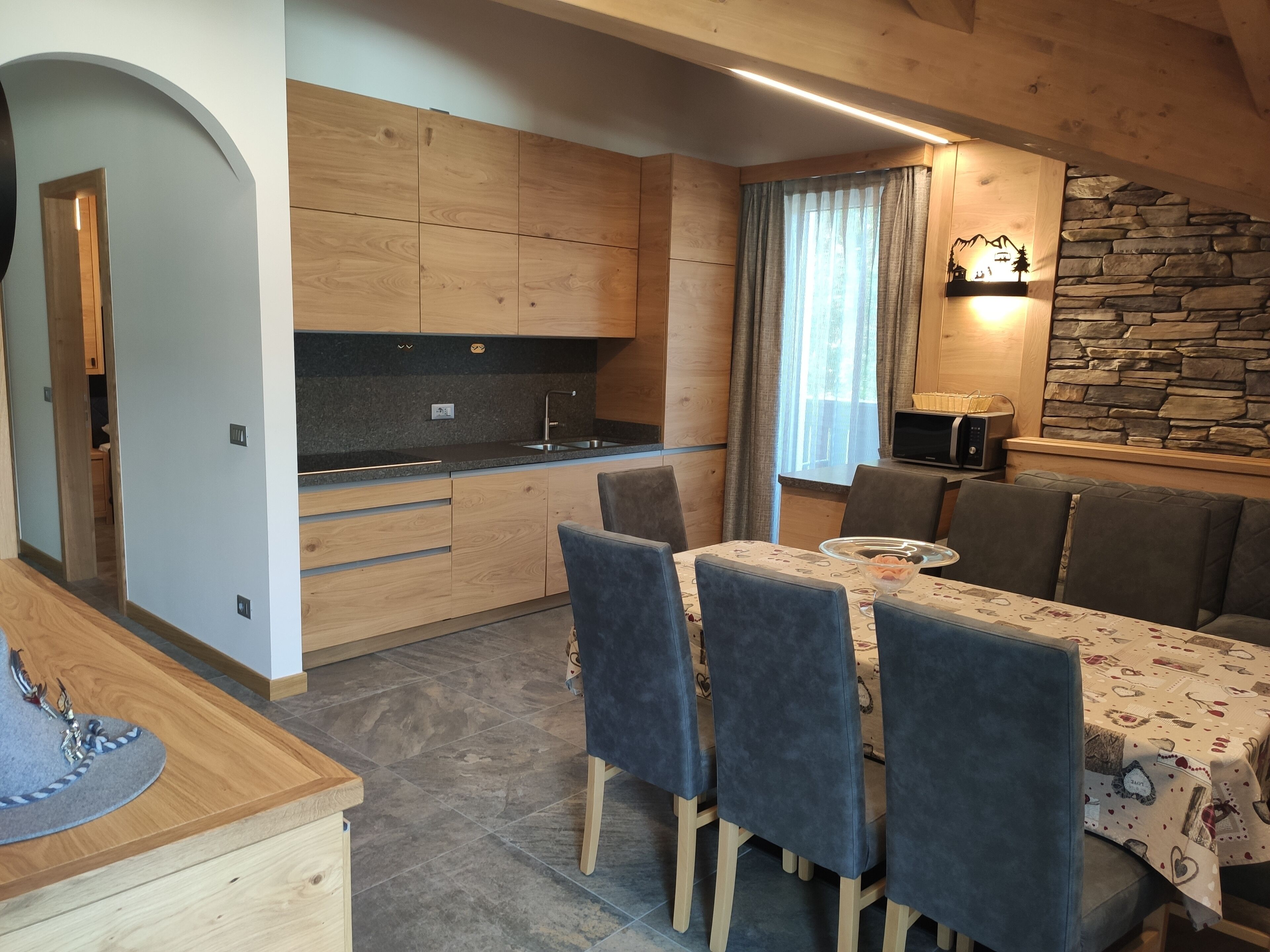 A modern kitchen with wooden cabinets, a built-in oven, and a dining area with a table and chairs.
