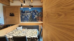 A dining area with a wooden table and chairs, a large mountain mural on the wall, and pendant lighting. - Appartamenti al Toscana (Andalo)