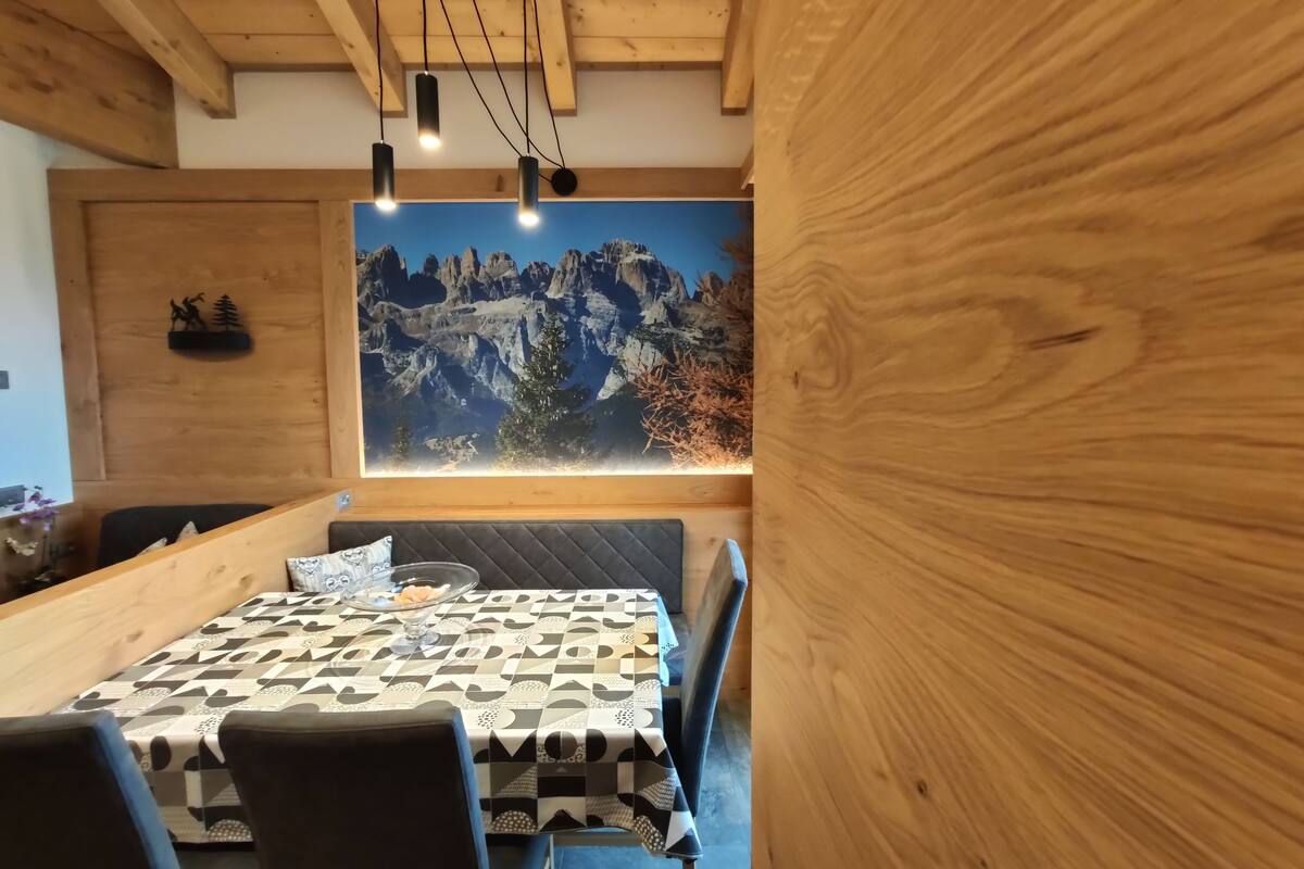 A dining area with a wooden table and chairs, a large mountain mural on the wall, and pendant lighting.