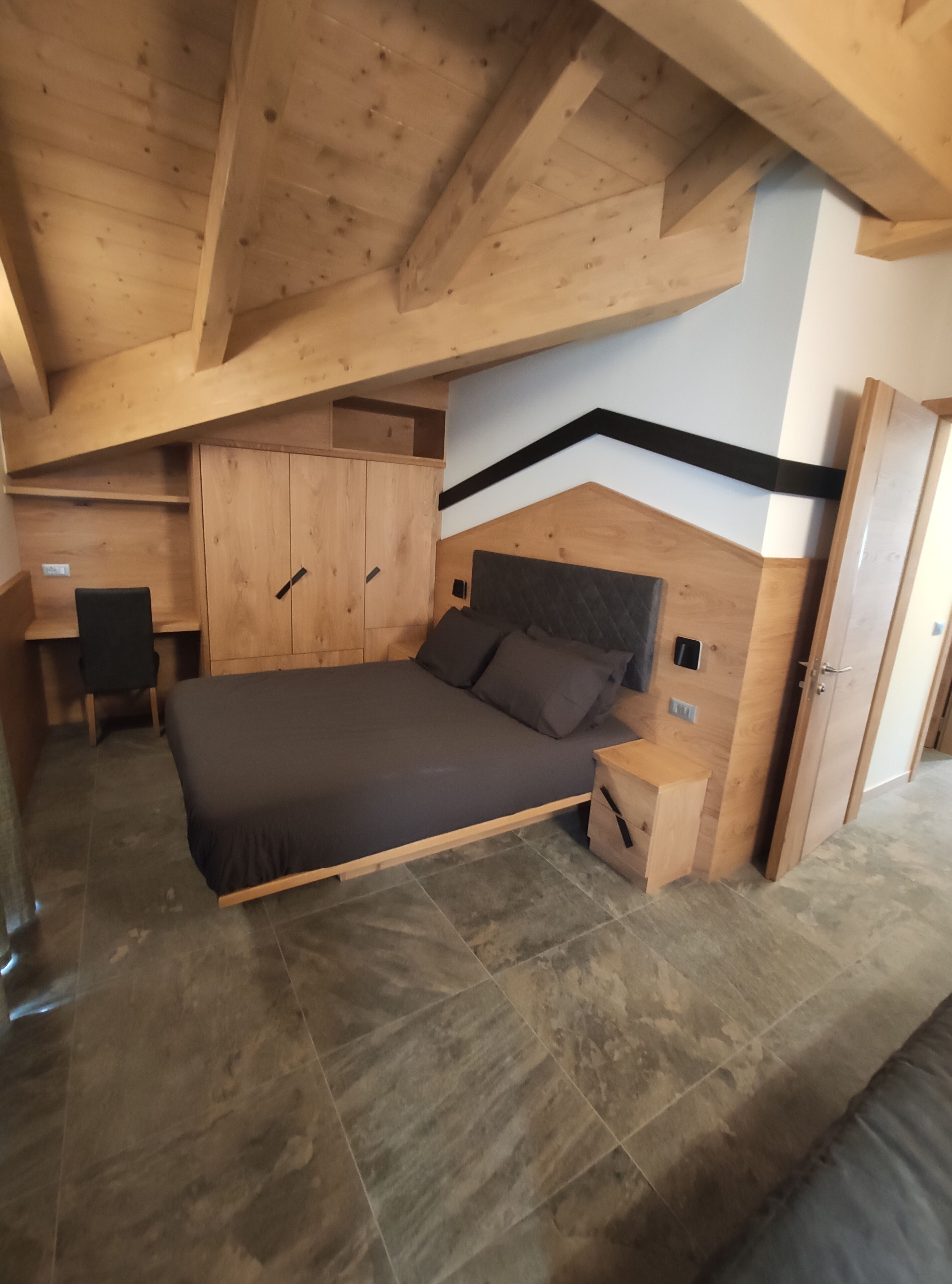 A bedroom with a wooden ceiling, a bed, a nightstand, a wardrobe, and a desk.