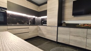 A modern kitchen with wooden cabinetry, a marble backsplash, and a flat-screen TV mounted above the counter. - Appartamenti al Toscana (Andalo)