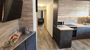 A modern kitchen with a flat-screen TV, a dining area, and a hallway leading to a living room. - Appartamenti al Toscana (Andalo)