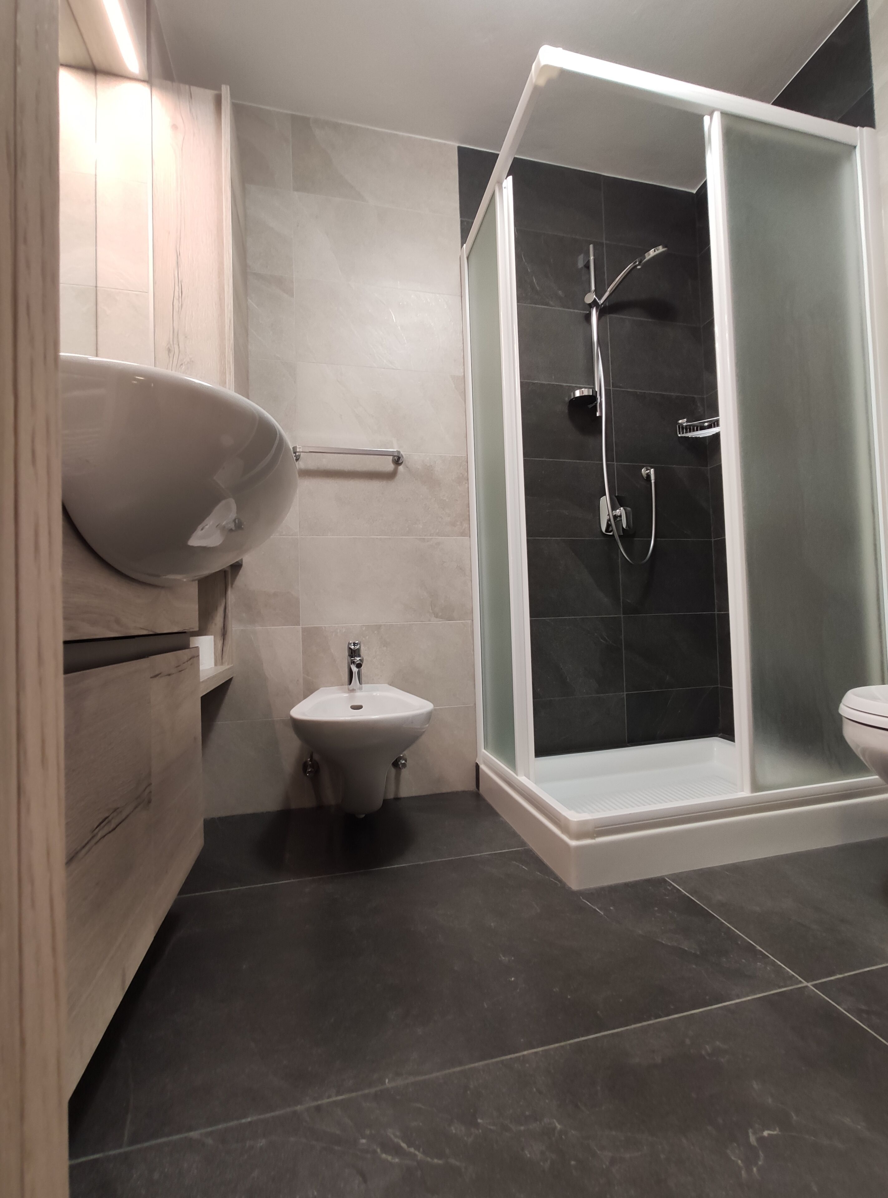 Een moderne badkamer met een douchecabine van glas, een wastafel op een voetstuk en een toiletbril met douchefunctie.