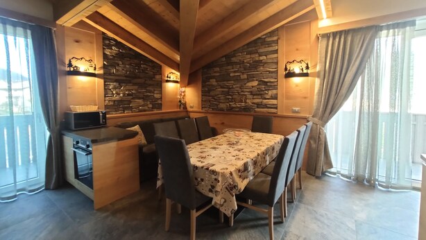 A dining area with a wooden table, chairs, and a stone wall. - Appartamenti al Toscana (Andalo)