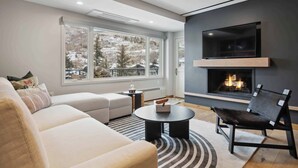 A modern living room with a fireplace, large windows, a sofa, and a coffee table. - Lodge Tower 486 2 BR at the base of Vail Mountain (Vail)