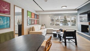 A modern living room with a sofa, coffee table, and dining table. There are framed artworks on the walls and a fireplace on the right. - Lodge Tower 486 2 BR at the base of Vail Mountain (Vail)