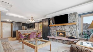A modern living room with a fireplace, comfortable seating, and a kitchen in the background.