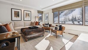 A spacious living room with a large window offering a mountain view, a fireplace, and a cozy seating area with leather sofas and a coffee table. - Lodge Tower 687 3BR at the base of Vail Mountain (Vail)