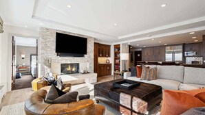 A modern living room with a stone fireplace, a flat-screen TV, and a kitchen area with dark cabinets and a stainless steel refrigerator. - Lodge Tower 687 3BR at the base of Vail Mountain (Vail)