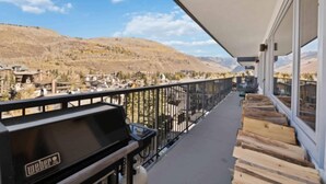 A balcony with a Weber grill, wooden steps, and a view of a mountainous landscape.