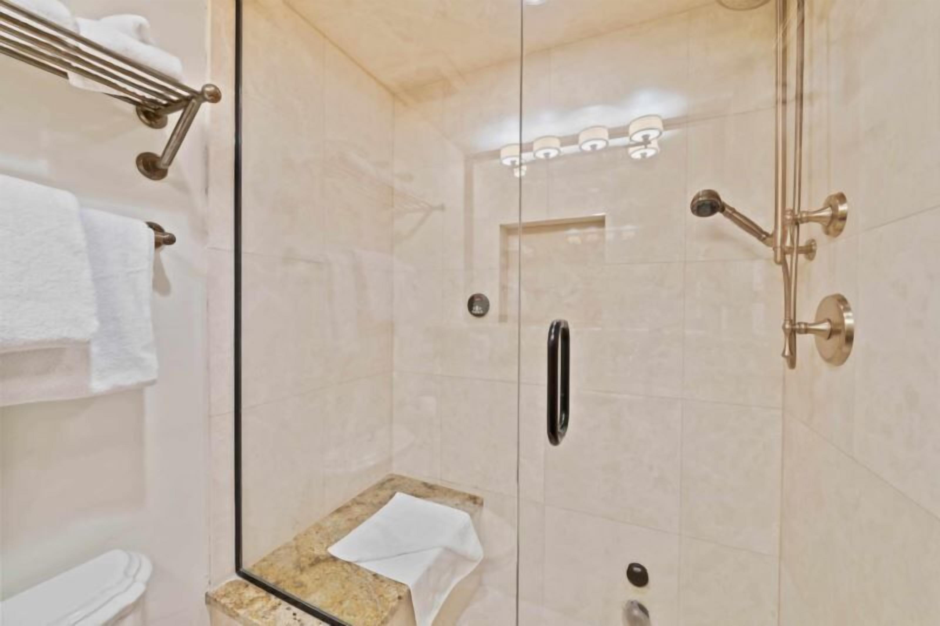Cabina doccia con pareti in vetro, piano di appoggio in marmo, portasciùmani e WC visibile sullo sfondo.
