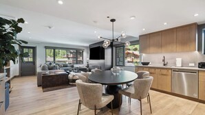 Een moderne keuken met houten kastjes, een eethoek met een ronde tafel en stoelen, en een zithoek met een bank en salontafel.