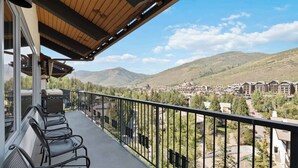 Ein Balkon mit Sitzgelegenheit im Freien, Blick auf eine Stadt und Berge, und eine Holzbalkendecke.