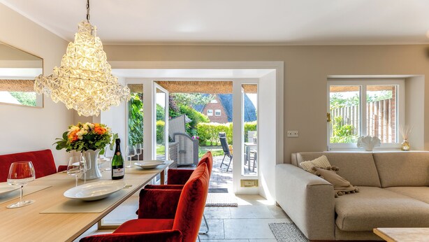 Un soggiorno moderno con zona pranzo, un divano in velluto rosso, un lampadario e vista sul giardino attraverso le porte in vetro.