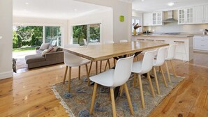 Eine moderne Küche mit weißen Schränken, einem Holztisch und einem großen Fenster mit Blick auf einen Garten.