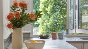 Eine Küche mit einem großen Fenster, einer Blumenvase, einer Obstschale und Holzschneidebrettern.