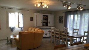 A living room with a sofa, dining table, and chairs. There is a kitchen area with cabinets and a refrigerator. - Maison Individuelle de Caractère (Roquebrune-sur-Argens)