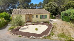 A house with a tiled roof, a stone archway entrance, a gravel driveway, and a garden with a heart-shaped flower bed. - Maison Individuelle de Caractère (Roquebrune-sur-Argens)