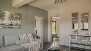 Een moderne woonkamer met een grijze bank, een salontafel en een schilderij van bomen. Er staat een console met decoratieve objecten en een spiegel erboven.