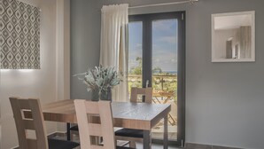 Een eethoek met een houten tafel en stoelen, een potplant en uitzicht op het buitenleven door een glazen deur.