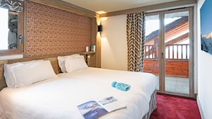A hotel room with a large bed, a wooden headboard, a red carpet, a view of a wooden balcony, and a wall-mounted light. - Hôtel L’Aigle du Montana by Les Etincelles (Tignes)