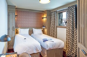 Ein Hotelzimmer mit zwei Betten, einem Holz-Kopfteil, einer Wand mit Muster, einem Fenster mit Vorhängen und einer Lampe.