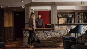 A reception area with a stone wall, a red door, and a bar counter with chairs. - Hôtel L’Aigle du Montana by Les Etincelles (Tignes)