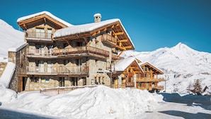 A multi-story stone building with wooden balconies, surrounded by snow and mountains. - Hôtel L’Aigle du Montana by Les Etincelles (Tignes)