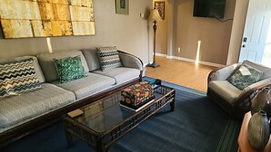 Een woonkamer met een bank, een salontafel, een stoel, een vloerlamp en een televisie.