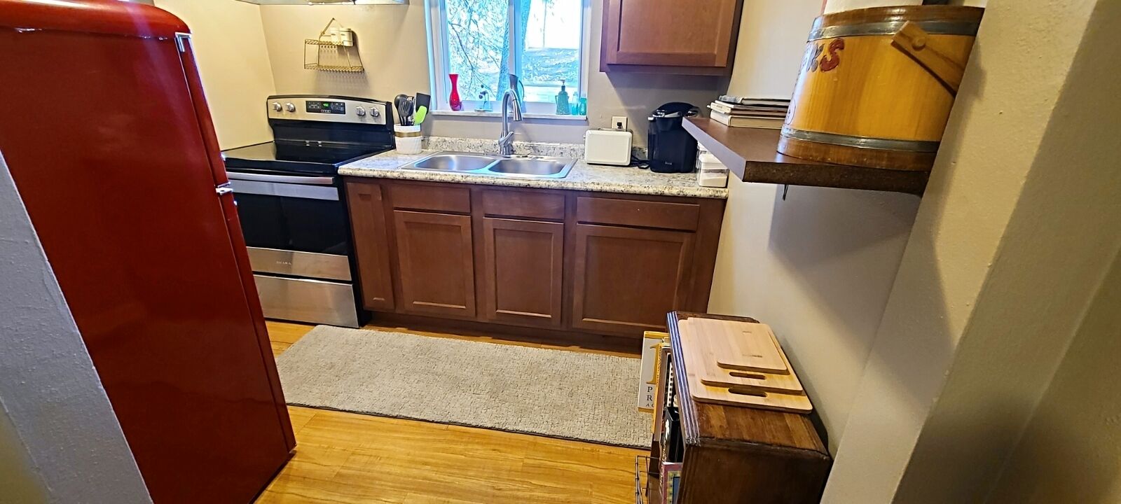 A compact kitchen with wooden cabinets, a stainless steel stove, a sink, and a coffee maker.