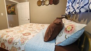 Een slaapkamer met een bed, een bloemenprint sprei, kussens, een wandklok en een deur.