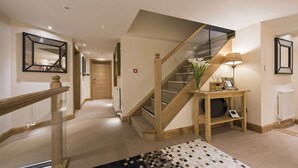 Un escalier avec des rampes en bois et un panneau de verre, menant à l’étage supérieur.