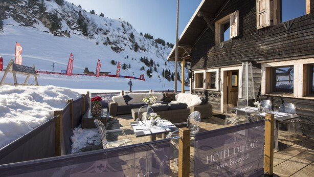 Un bâtiment en bois doté d’une terrasse aménagée avec des sièges et des tables extérieures.