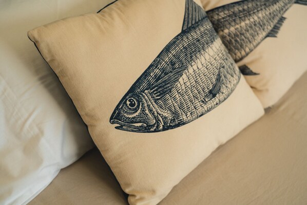 Un coussin beige orné d’une illustration représentant un poisson noir, posé sur un canapé beige.