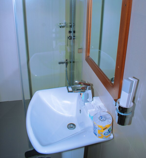 A bathroom with a white sink, a glass shower enclosure, and a wooden-framed mirror.