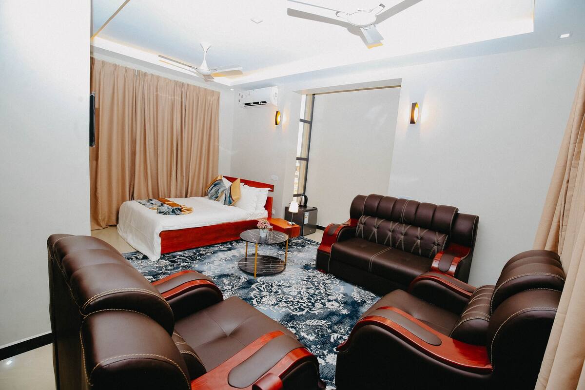 Une chambre d’hôtel avec un lit, deux canapés, une petite table, un ventilateur de plafond et une grande fenêtre.