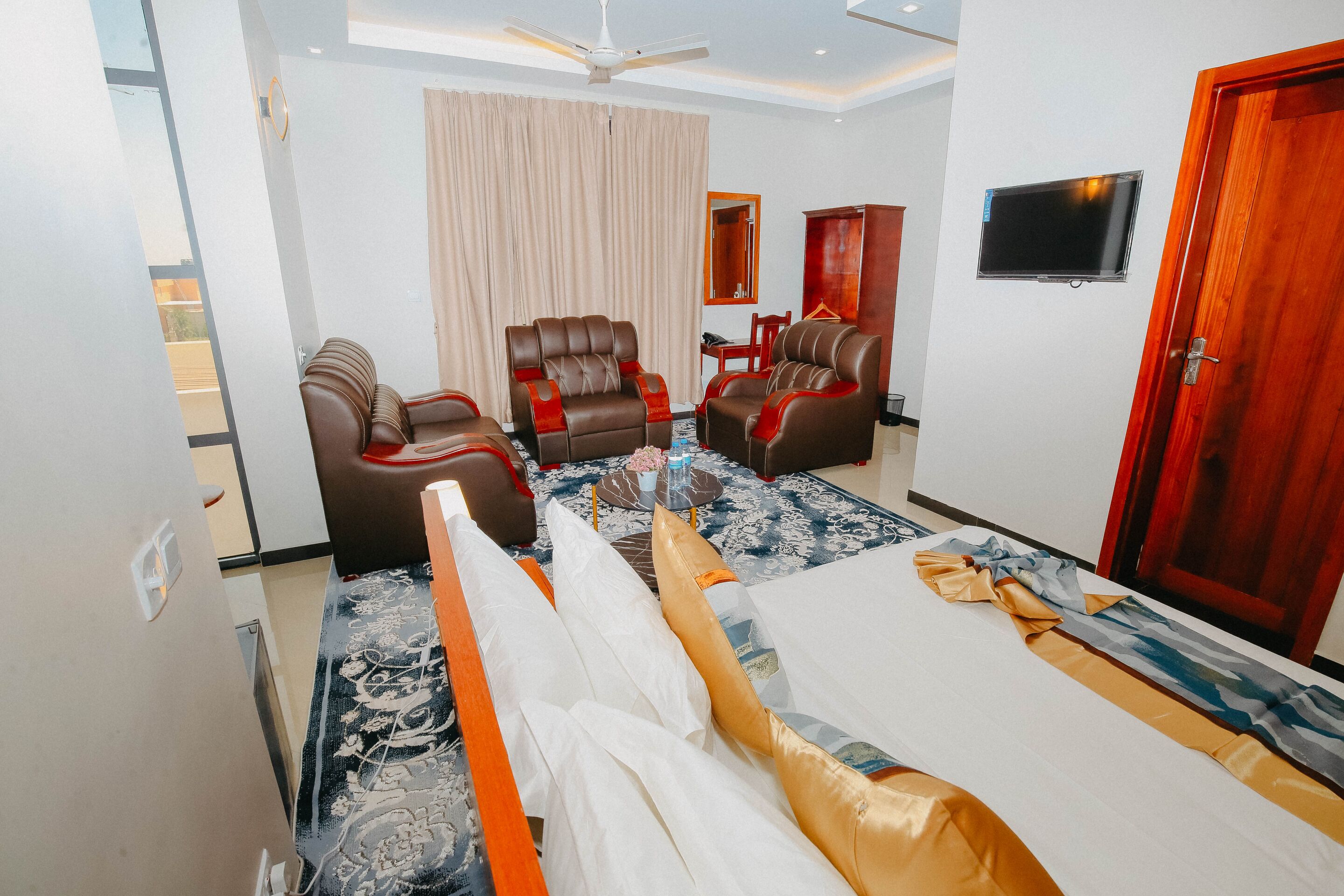 A hotel room with a bed, two leather armchairs, a sofa, a television, and a ceiling fan.