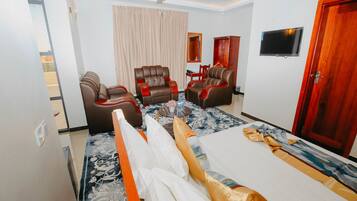 Une chambre d’hôtel comprenant un lit, deux fauteuils en cuir, un canapé, une télévision et un ventilateur de plafond.