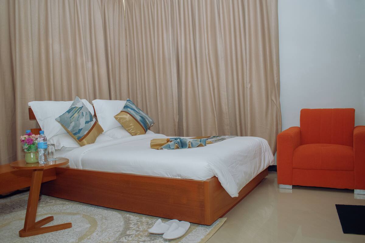 Une chambre à coucher avec un lit en bois, une table de chevet ornée d’un vase de fleurs et un fauteuil orange vif.