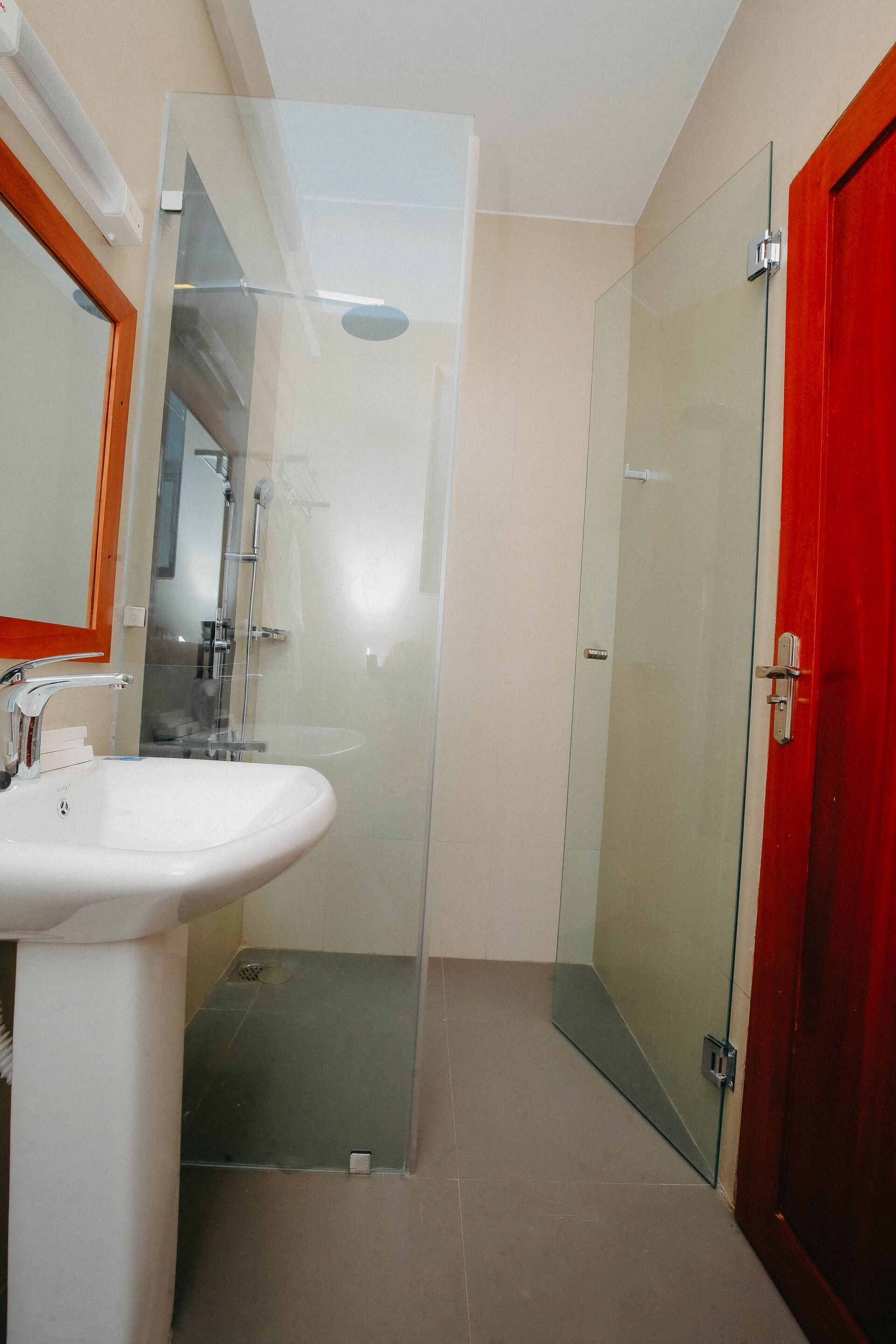Casa de banho com cabine de chuveiro em vidro, pia branca e porta vermelha.