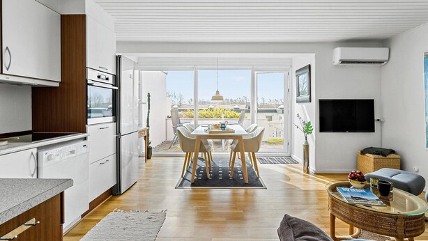 Een moderne keuken met witte kasten, een eethoek met tafel en stoelen, en een zithoek met televisie en rieten meubilair.