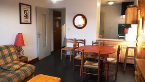Una sala de estar con un sofá, una mesa de madera y un comedor con una mesa redonda y sillas. Se ve una cocina al fondo.